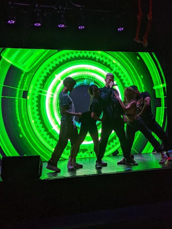 Image of Performer and back up dancers standing in front of large LED Display