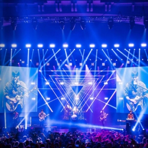 Image of band performing on main stage with vibrant visuals, lights, and audience.